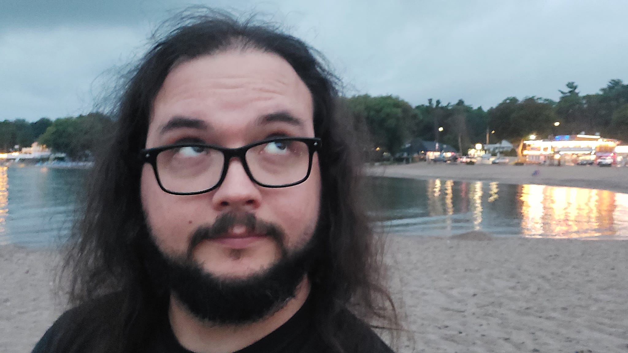 A man with long dark hair and a beard is at a sandy beach with a granite boulder breakwater, photo 6